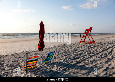 Bunt gestreifte Strand Klappstühle und gefalteten roten Regenschirm mit orange Leben bewachen Stühle und Atlantischen Ozean hinaus sichtbar. Stockfoto