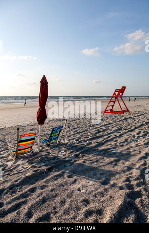 Bunt gestreifte Strand Klappstühle und gefalteten roten Regenschirm mit orange Leben bewachen Stühle und Atlantischen Ozean hinaus sichtbar. Stockfoto