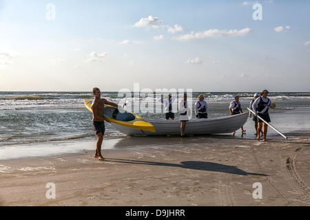 Junger Mann mit seinem Seekajak aus dem Meer mit Ocean Rescue Boot und freiwilligen Helfern im Hintergrund. Stockfoto