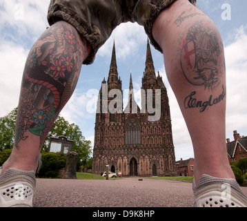 Ungewohnter Anblick der Westfassade der Kathedrale von Lichfield gesehen durch Mannes tätowierten Beine die ewig England lesen Stockfoto