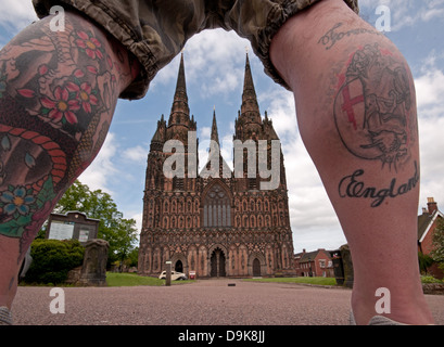 Ungewohnter Anblick der Westfassade der Kathedrale von Lichfield gesehen durch Mannes tätowierten Beine die ewig England lesen Stockfoto