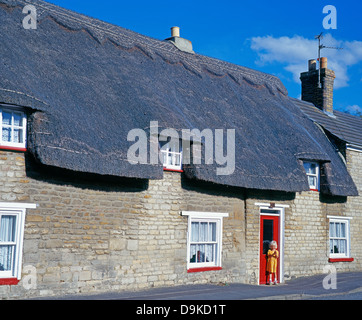 Eine hübsche, blonde, drei Jahre altes Mädchen, außerhalb der roten Front Tür einer strohgedeckten Hütte im Deeping St James, Lincolnshire, England, Vereinigtes Königreich. Stockfoto