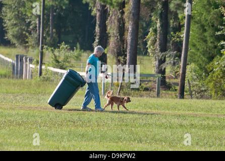 Ländliche Hausfrau tut doppelte Pflicht, dem Hund spazieren gehen, während in die Mülltonne bringen. Stockfoto