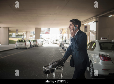 Junger Mann auf Handy mit Gepäckwagen am Flughafen Stockfoto