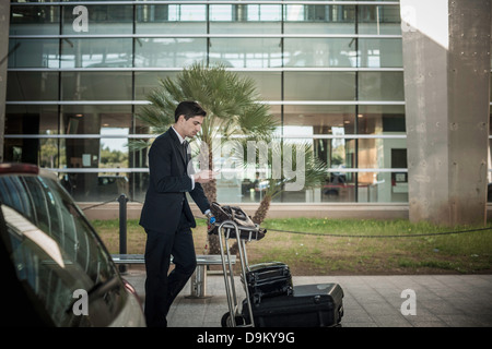 Junger Mann mit Handy mit Gepäckwagen am Flughafen Stockfoto