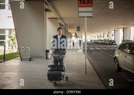 Junger Mann mit Gepäckwagen am Flughafen Stockfoto