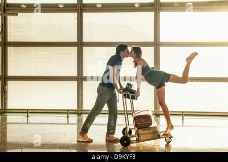 Junges Paar mit Gepäck Wagen küssen im Flughafen Stockfoto