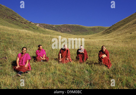 Tibetische buddhistische Mönche im roten Kleid machen eine Pause auf einem Hügel am Rande der kleinen Bergstadt Langmusi am östlichen Rand des Qinghai-Plateaus, eingebettet in ein Tal, das sich zwischen den Provinzen Gansu und Sichuan in China teilt Stockfoto