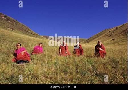 Tibetische buddhistische Mönche im roten Kleid machen eine Pause auf einem Hügel am Rande der kleinen Bergstadt Langmusi am östlichen Rand des Qinghai-Plateaus, eingebettet in ein Tal, das sich zwischen den Provinzen Gansu und Sichuan in China teilt Stockfoto