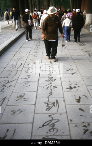 Ein Mann nutzt einen manipulierten riesigen Pinsel Tinte Wasser verdunstet wie Kalligraphie, die verschwindende Tinte auf der Fahrbahn in Summer Palace Beijing China zu schreiben. Stockfoto