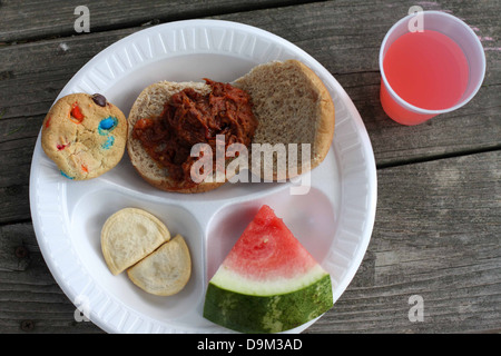 weißen Teller mit Essen bei Picknick, Barbecue-Sandwich auf Roll, Cookie, Wassermelone, rosa Punsch trinken im Cup, Platte auf Holztisch Stockfoto