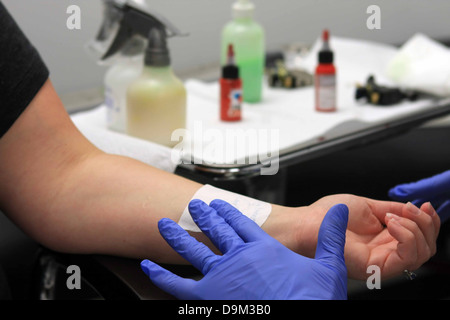 Person, die bereit sind, ein Tattoo auf dem linken Handgelenk, Künstler mit blauen Handschuhen mit Schablone liefert im Hintergrund, Künstler Stockfoto