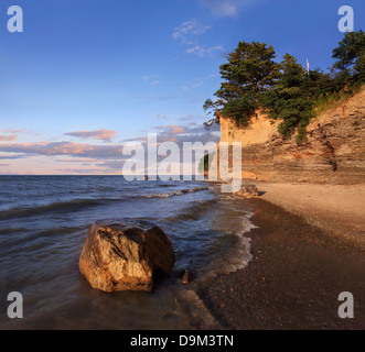 Ein Findling sitzt In der Brandung mit Klippen hinter strahlenden Morgenlicht, Erie-See am Strand von Barcelona, New York, USA Stockfoto