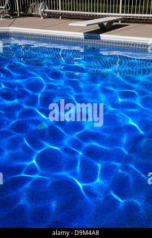 Ein Sprungbrett und tiefblaue Schwimmbadwasser bilden abstrakte Muster erstellt von Sonnenlicht auf die wellige Oberfläche tanzen Stockfoto