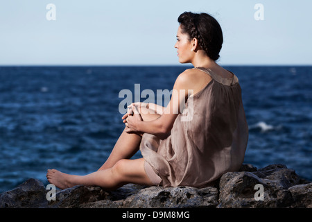Hübsche junge Frau sitzt auf den Felsen mit Blick auf Meer Stockfoto