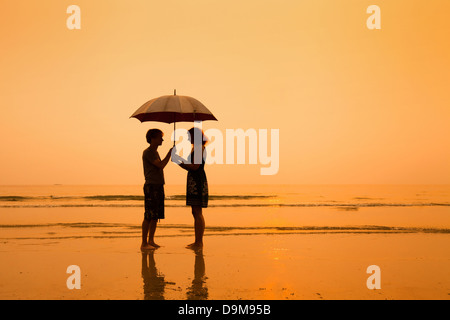 Familie am Strand, Silhouetten des Paares mit Regenschirm Stockfoto