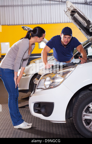 Kfz-Mechaniker im Gespräch mit weiblichen Kunden vor ihrem Auto mit Motorhaube öffnen Stockfoto