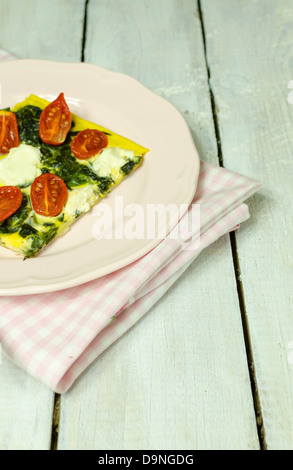 Spinat und Tomaten-Tarte mit Feta-Käse auf einem rosa Teller Stockfoto