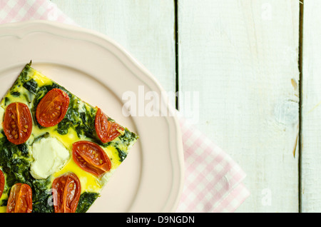 Spinat und Tomaten-Tarte mit Feta-Käse auf einem rosa Teller Stockfoto