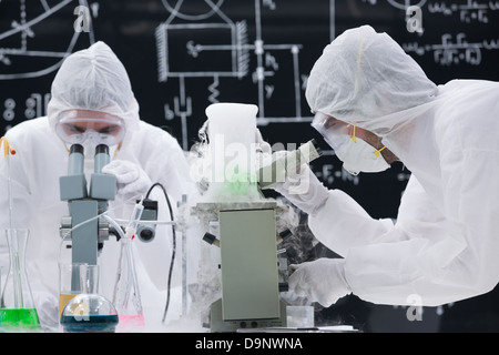 Nahaufnahme der beiden Wissenschaftler analysieren unter Mikroskop in einem Chemielabor mit einer Tafel auf dem Hintergrund Stockfoto