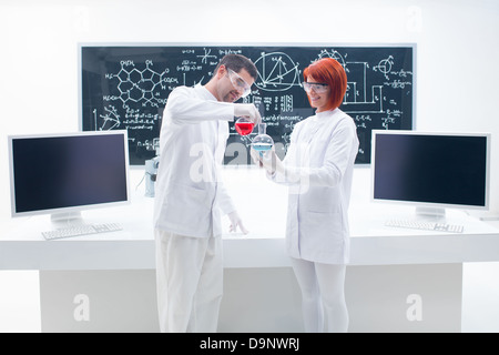 allgemeine Ansicht von zwei Personen in einem Chemielabor hält eine Grapefruit mit einer Spritze und einem Arbeitstisch und Tafel auf dem ba Stockfoto