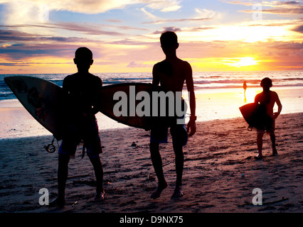 Lokalen Jungs mit einem Surfbretter bei Sonnenuntergang am Strand. Bali, Indonesien Stockfoto