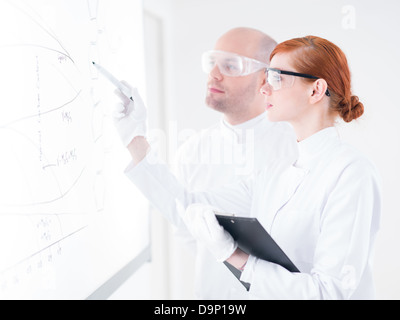 Seitenansicht eines Schülers zeigt Grafiken auf einem White-Board, während seines Lehrers ihr beaufsichtigt Stockfoto