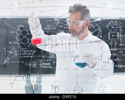 Nahaufnahme der Wissenschaftler, die Durchführung von chemischen Laborexperimenten mit bunten Flüssigkeiten und eine Tafel mit Formeln auf dem ba Stockfoto