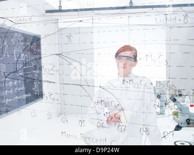 allgemeine Ansicht eines Schülers in einem Chemielabor analysieren, Formeln und Grafiken auf einer transparenten Tafel Stockfoto