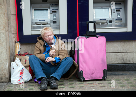 Obdachloser mit hab und gut essen Eis vor Natwest Geldautomaten in London City - UK Stockfoto