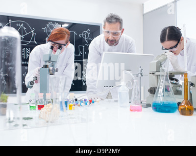 allgemeine Ansicht von zwei Studenten in ein Chemie-Labor-Analyse unter Mikroskop unter Aufsicht eines Lehrers Stockfoto