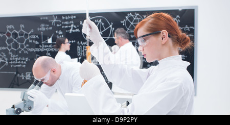 Nahaufnahme eines Studenten in Chemie-Labor führt ein Experiment mit bunten Iquids und eine weitere drei Personen, die Analyse von Daten Stockfoto