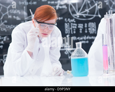 Nahaufnahme eines Schülers in einem Chemielabor, die Durchführung eines Experiments mit bunten Flüssigkeiten und Gas auf einem Labortisch mit einem Blackboard-o Stockfoto