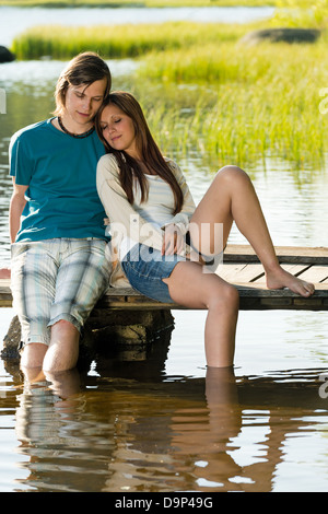 Teen Paar sitzt am Pier mit den Beinen im Wasser Stockfoto
