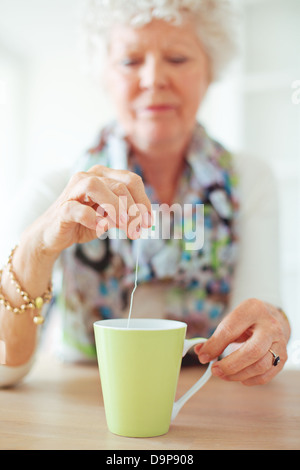 Alte Dame sitzt zu Hause halten und Dippen einen Teebeutel Stockfoto