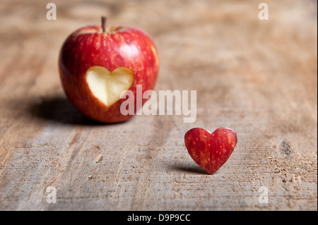 Roter Apfel mit Herz-Form ausschneiden. Die ausgeschnittenen Herzen vor/neben der Apfel eine Warm getönten Holzoberfläche im Vordergrund. Liebe Stockfoto