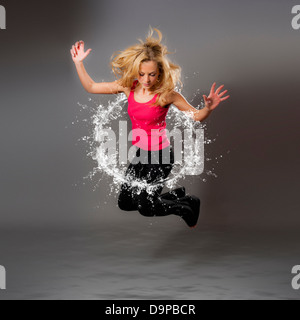 Zusammengesetzte Aufnahme einer jungen kaukasischen Frau, die durch einen kreisförmigen Wasserspritzer springt Stockfoto