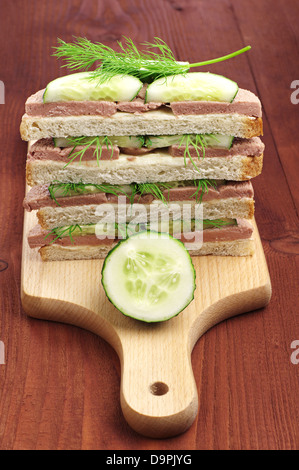 Brötchen mit Leberwurst und Gurke auf Schneidebrett auf einem Holztisch Stockfoto