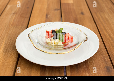 Caprese Tomaten und Mozzarella-Tartar in Glasplatte auf einem Holztisch. Stockfoto