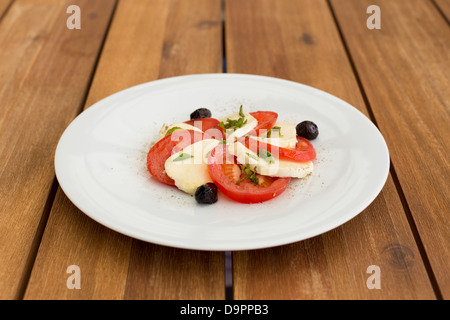 Frischer Mozzarella, Tomaten-Salat in weißer Teller auf einem Holztisch. Stockfoto