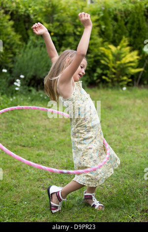 Lächelnde Mädchen spielen mit Hula-Hoop in ihrem Garten. Stockfoto