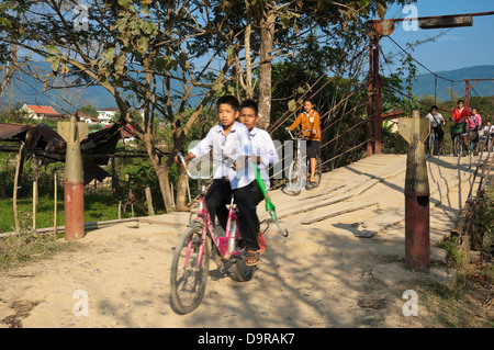 Horizontale Porträt des laotischen Kinder reiten auf ihre Fahrräder über eine Brücke mit Bombe Casting Poller in Vang Vieng. Stockfoto