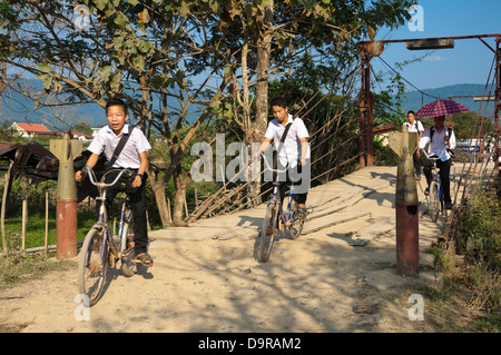 Horizontale Porträt des laotischen Kinder reiten auf ihre Fahrräder über eine Brücke mit Bombe Casting Poller in Vang Vieng. Stockfoto