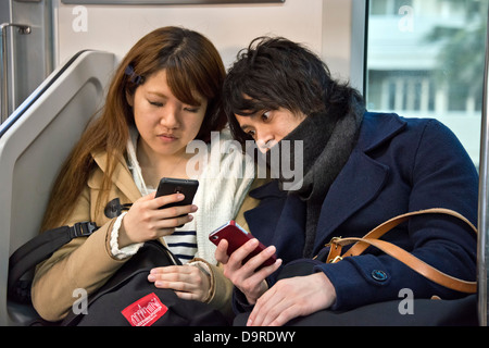 Junges Paar mit Mobiltelefonen auf Tokyo Metro Stockfoto