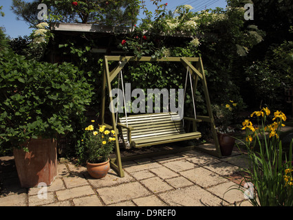 Garten Schaukelsitz vor einem Klettern Hortensien und Rosen, die ein Gartenhaus zu verbergen. Gelbe Schwertlilien auf der rechten Seite Stockfoto