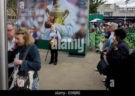 Wimbledon, England, 25. Juni 2013 - Tag2 der Zuschauer und der jährlichen Lawn Tennis Championships mischen sich mit Einheimischen in der Nähe einer großen Champions Trophy Plakatwand, außerhalb der Hauptstrecke und Underground (u-Bahn) Station in den südlichen Vorort von London. Der Wimbledon Championships, das älteste Tennisturnier der Welt, haben seit 1877 an der nahe gelegenen All England Club statt. Stockfoto