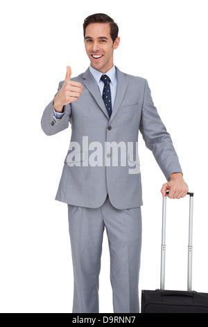 Lächelnde Geschäftsmann mit seinem Daumen auftauchend Koffer Stockfoto