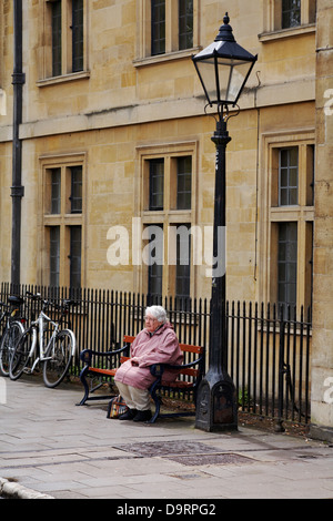 Im Mai saß eine ältere Frau in Oxford, Oxfordshire, Großbritannien, an einem Laternenpfahl auf der Bank Stockfoto
