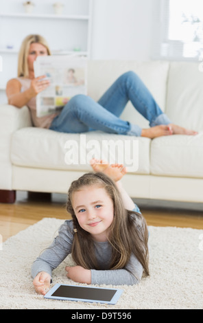 Lächelndes Mädchen mit Tablet, während ihre Mutter Zeitung liest Stockfoto