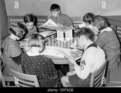 Mädchen und jungen an einem Tisch sitzen und lesen Sie Bücher in der Kinder Lesesaal einer Bibliothek in Berlin, Deutschland. Ein Junge trägt die Uniform der deutschen Jugend mit einer einfachen Sieg-Rune auf der Zunge. Datum unbekannt. Der NS-Propaganda! auf der Rückseite des Bildes liest: "in der kommenden Woche des deutschen Buches. Ein Kinder Lesesaal und seine kleinen Stammgäste. Von 25 Oktober bis 1 November dauert die Woche des deutschen Buches dieses Jahr statt, deren Ziel ist es, Buch und Menschen zusammenzubringen. -Bild Archiv: Ansicht eines Kinder der Lesesaal in Berlin: die jüngste Generation sitzt friedlich an die Ro Stockfoto